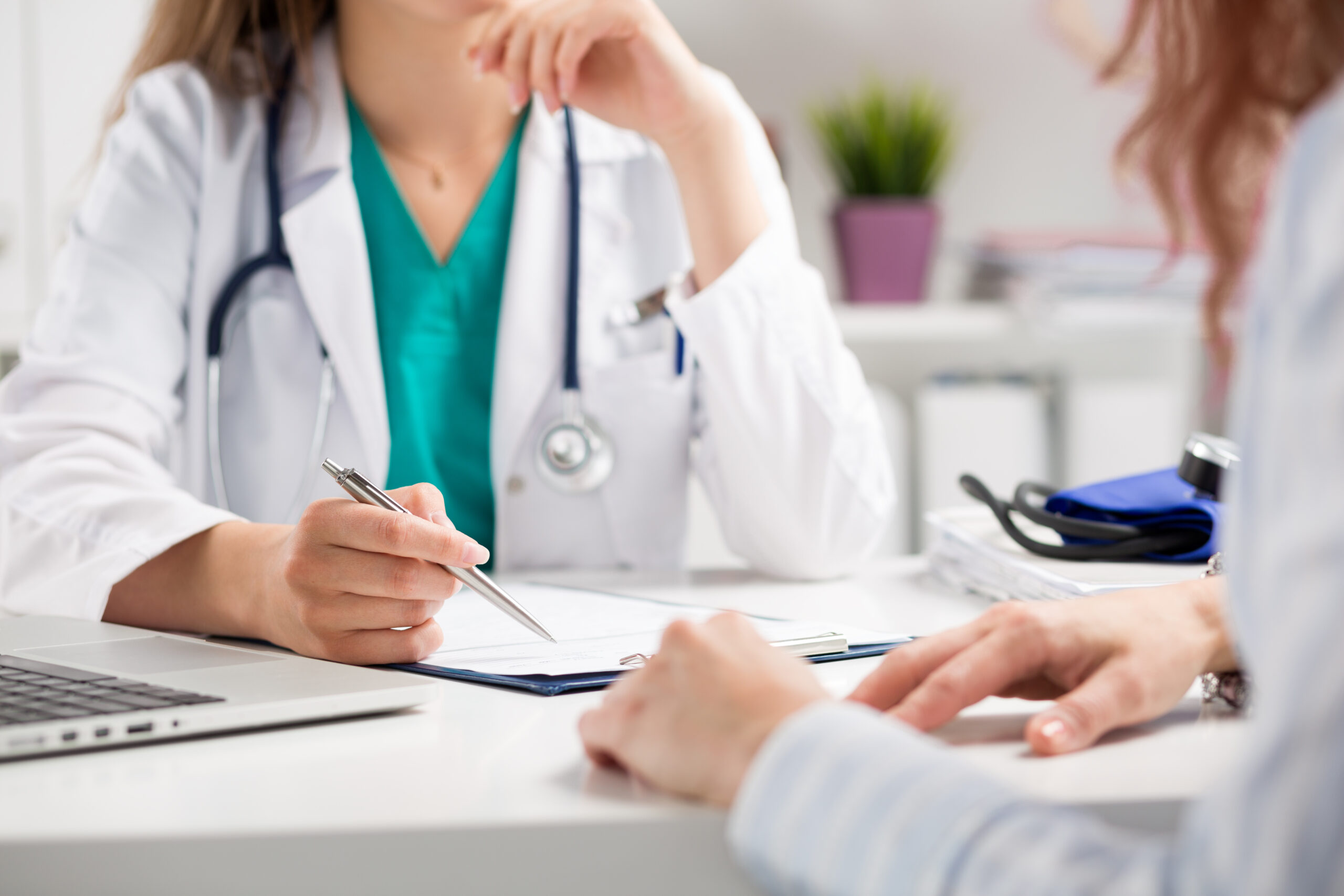 Ärztin mit Stethoskop erklärt einer Patientin medizinische Unterlagen während eines Beratungsgesprächs am Schreibtisch