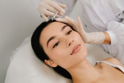 Eine Frau liegt auf einer Behandlungsliege, während eine medizinische Fachkraft mit Handschuhen eine Injektion in die Kopfhaut durchführt.